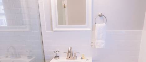 Un baño con lavamanos blanco, espejo, inodoro, cabina de ducha de vidrio y suelo de madera.