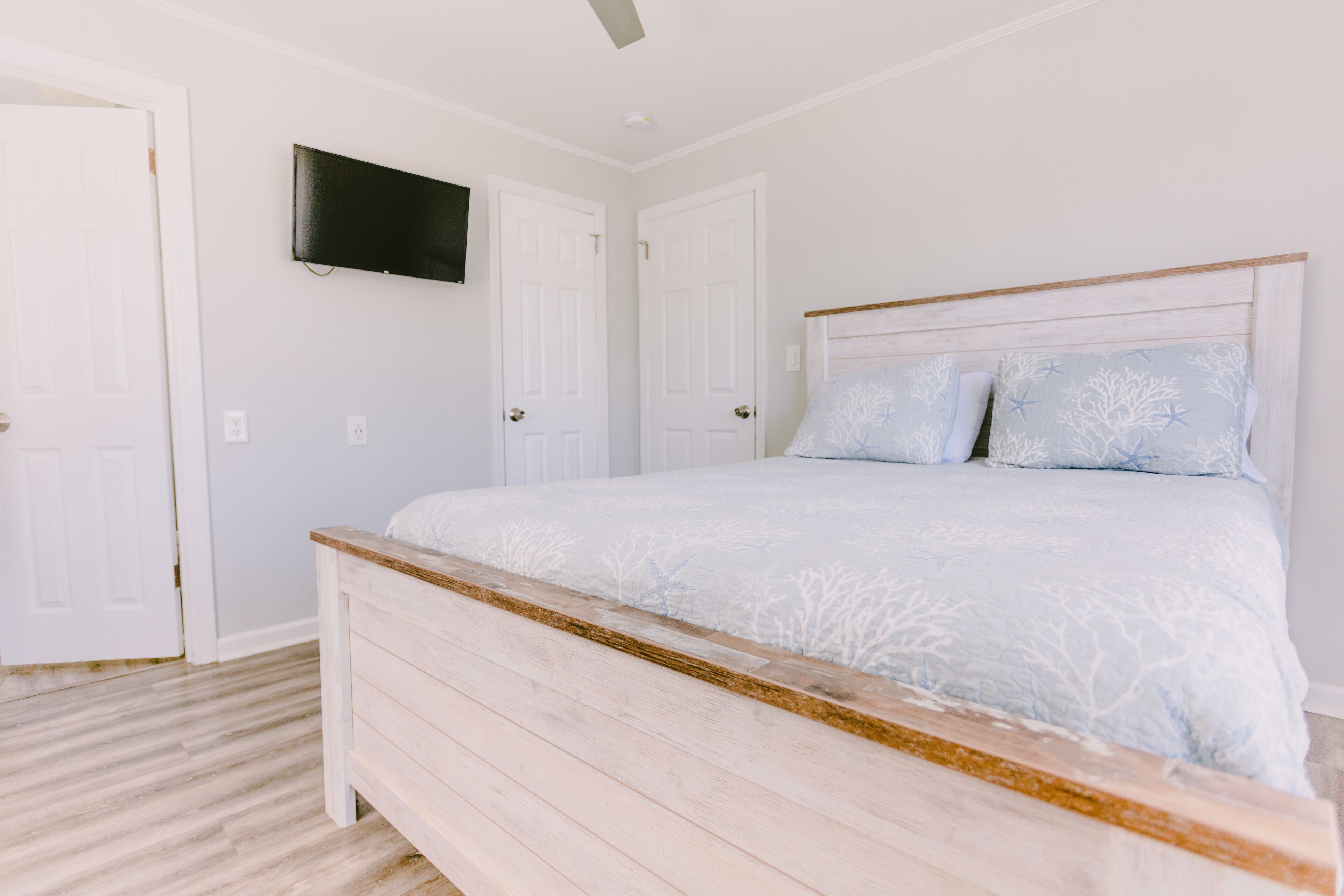 A bedroom with a bed, a television mounted on the wall, and two white doors.