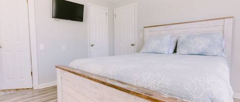 A bedroom with a bed, a television mounted on the wall, and two white doors.