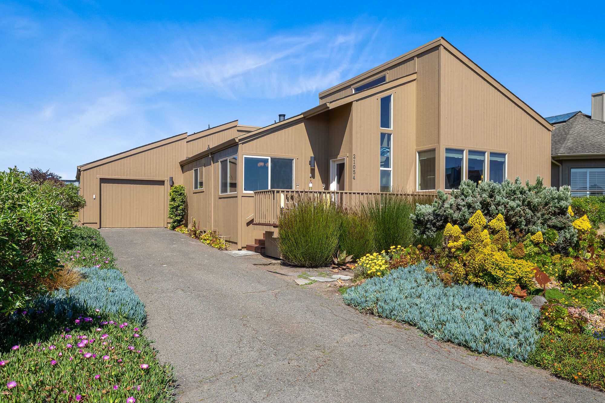 A modern two-story house with a driveway leading to the entrance, surrounded by landscaped gardens.