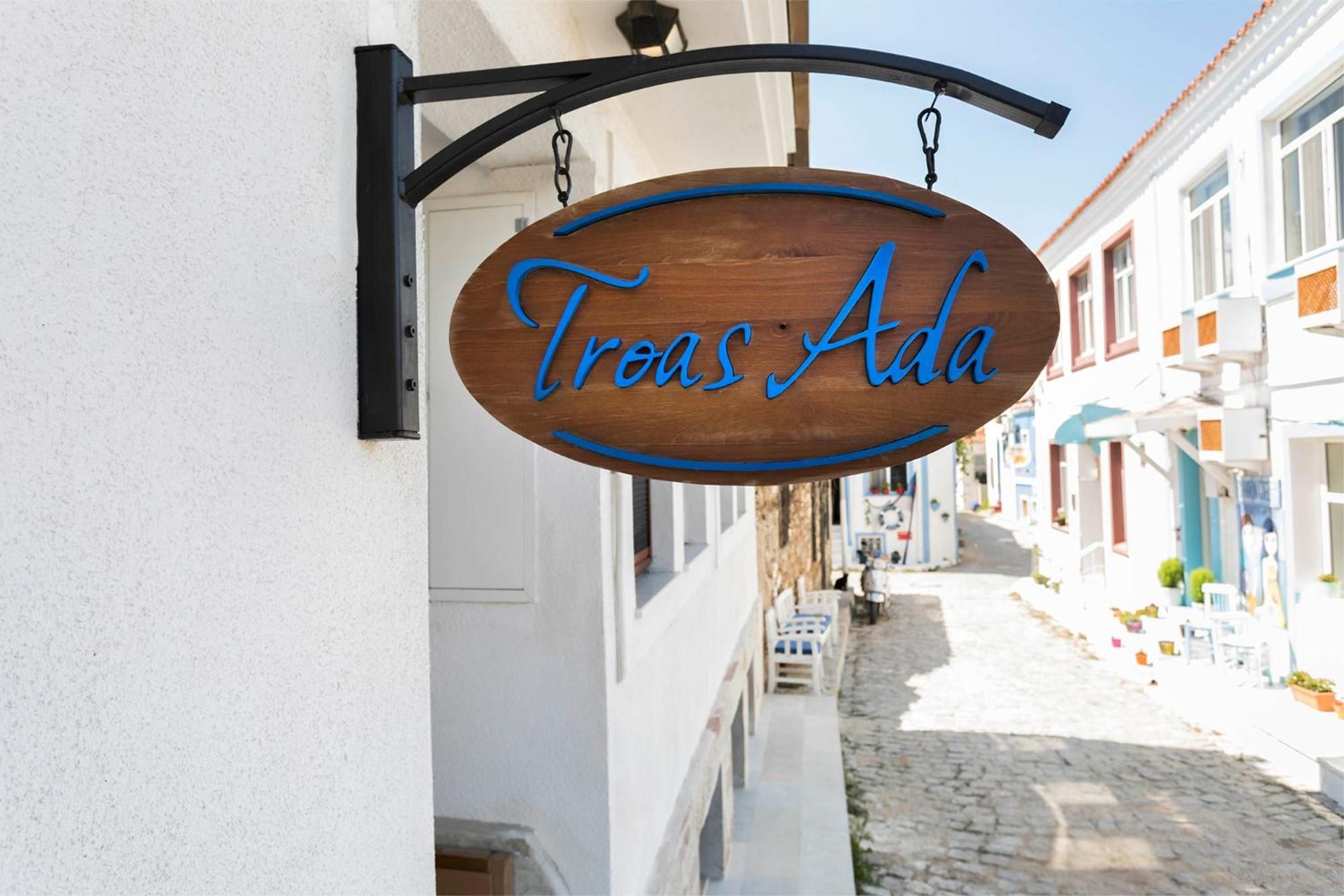 A wooden sign with the inscription 'Tres Ada' hanging from a black metal bracket.