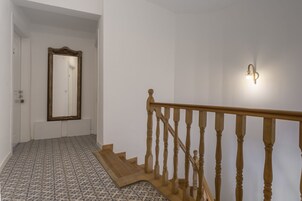 Una escalera con balaustres de madera y barandilla, que lleva a una habitación con suelo estampado y un espejo grande en la pared.