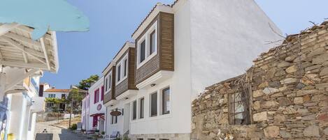 Una estrecha calle adoquinada con edificios tradicionales, muros de piedra y mesas al aire libre.