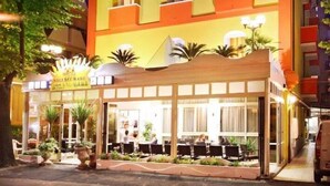 A hotel with a yellow facade, multiple balconies, and a covered outdoor seating area with tables and chairs.