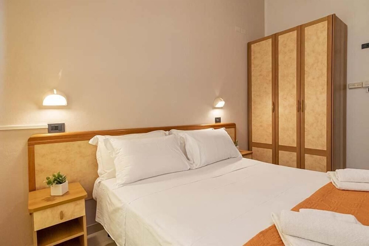 A hotel room with a bed, bedside tables, a wardrobe, and wall-mounted lights.