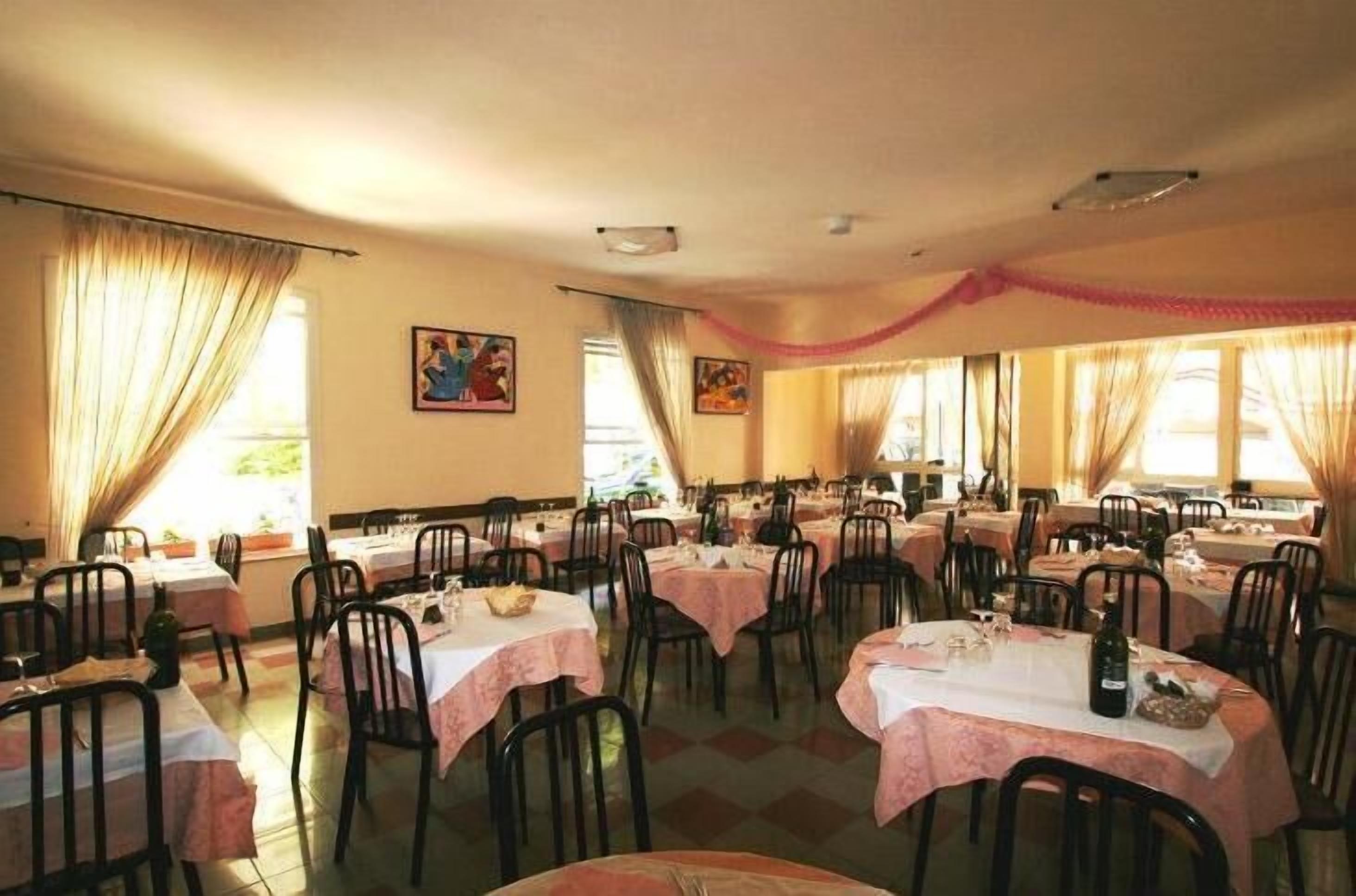 A dining area with round tables covered with white tablecloths, black chairs, and a warm, inviting atmosphere.