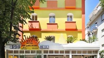 Un hôtel à la façade jaune vif, doté de nombreux balcons et d’un espace d’entrée couvert avec des sièges en plein air.