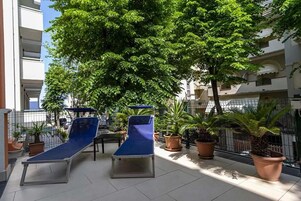 A rooftop terrace with two sun loungers and several potted plants.