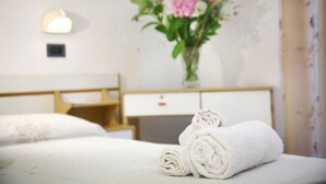 A hotel room with a neatly made bed, a desk with a lamp, and a vase of flowers on the wall.