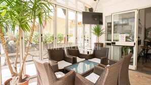 A sunlit indoor patio with wicker furniture, a glass-top table, and potted plants.
