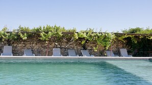 A pool area with striped lounge chairs and a stone wall with greenery. - La Glacière - Ostalarià Agricol (Tresques)