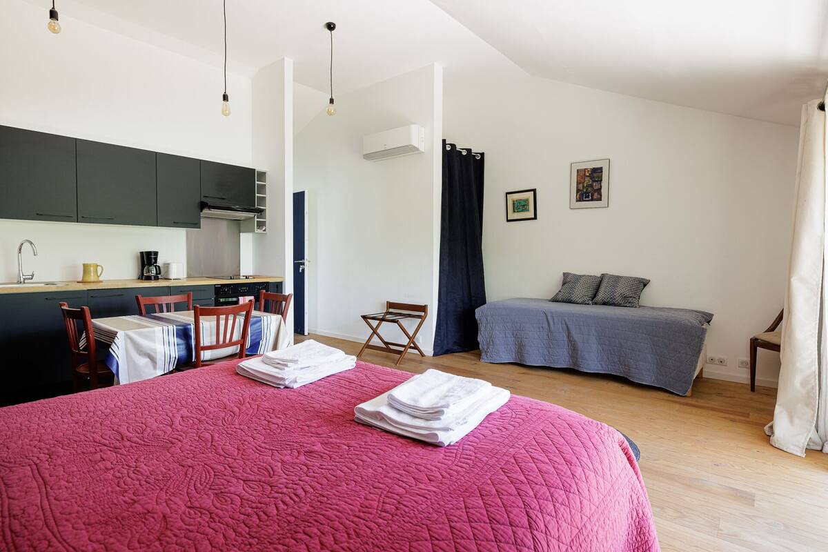 A compact bedroom with a bed, a small desk area, and a kitchenette.
