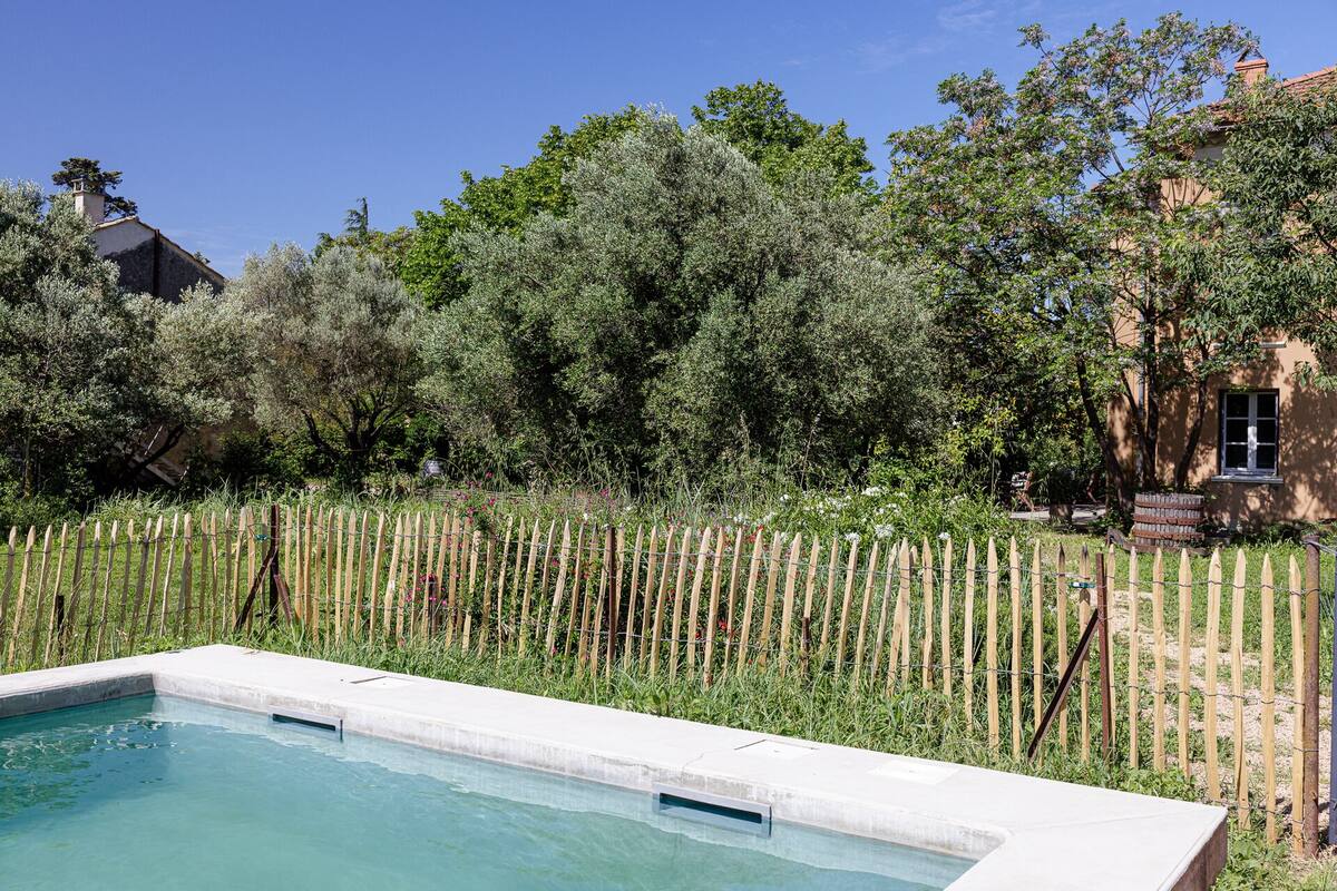 A swimming pool with a wooden fence and lush greenery in the background.