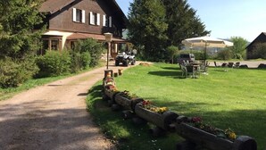 Una casa rústica con un camino de tierra que lleva a un espacio cubierto con mesas al aire libre.