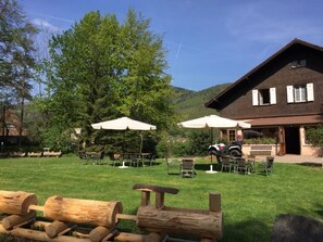 A lodge with outdoor seating, a mountain backdrop, and a large building with a sloped roof. - Le Chalet - Hotel Restaurant (Luttenbach-pres-Munster)