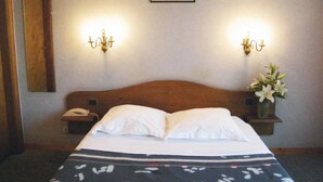 Habitación de hotel con cabecera de madera, cama con ropa blanca, dos mesitas de noche con lámparas y un cuadro enmarcado en la pared.