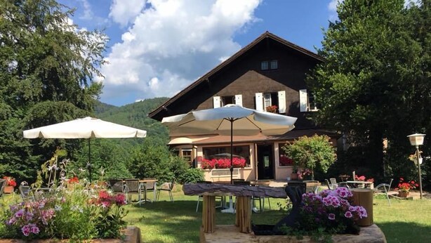 Un lodge rústico con fachada de madera, asientos exteriores y un jardín lleno de flores.