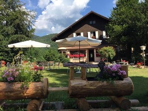 A rustic lodge with a wooden facade, outdoor seating, and a garden with flowers. - Le Chalet - Hotel Restaurant (Luttenbach-pres-Munster)