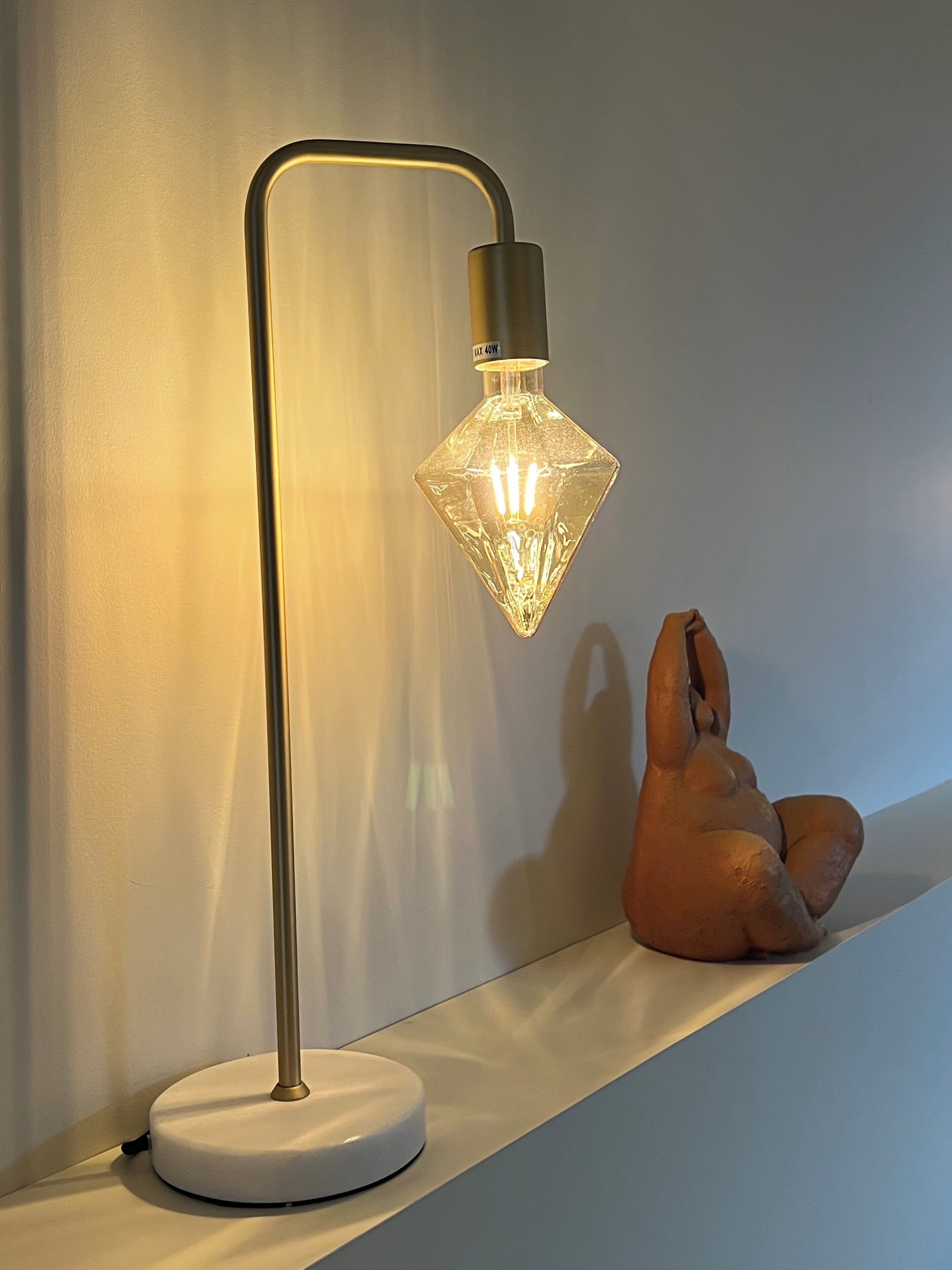Une lampe de bureau moderne dotée d’un abat-jour en verre aux formes géométriques et d’un pied métallique.