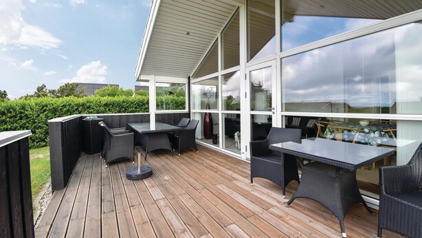An outdoor patio with a wooden deck, black wicker furniture, and large glass windows offering views of the sky and surrounding greenery. - Gorgeous home in Faaborg with WiFi (Faaborg)
