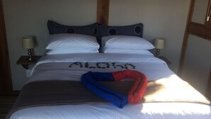 A bed with white bedding, a blue and red towel, and a pillow with a pattern.