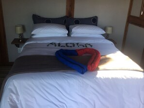 A bed with white bedding, a blue and red towel, and a pillow with a pattern.