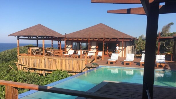 Une terrasse en bois avec une piscine, des chaises longues et un espace abrité offrant une vue sur l’océan.