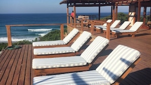 Une terrasse en bois avec des chaises longues et un espace salon couvert, offrant une vue sur l’océan.