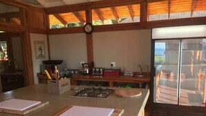 Une cuisine dotée de plans de travail en bois, d’une cuisinière à gaz, d’un réfrigérateur et d’une grande fenêtre donnant sur une terrasse.