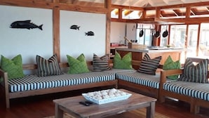 Une pièce chaleureuse avec un banc en bois et des coussins, une petite table sur laquelle se trouve un bol de biscuits, et un coin cuisine avec des ustensiles suspendus.