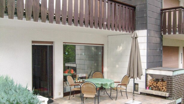 Une terrasse extérieure avec une table et des chaises, une clôture en bois et une cheminée en briques.