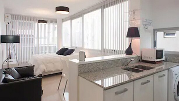A modern kitchen with a central island, built-in appliances, and a large window providing natural light. - HOMETANGO ABASTO (CABA)