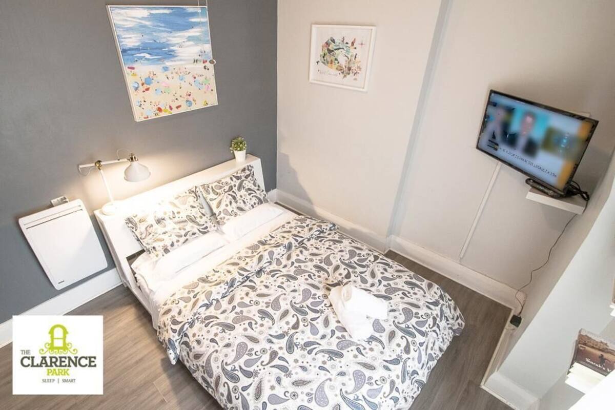 Een slaapkamer met een bed, nachtkastje, lamp, televisie en een klein plankje met een plant.