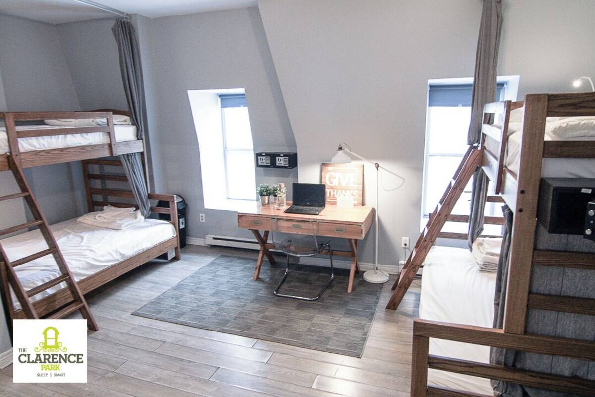 Een slaapzaal met stapelbedden, een bureau met een laptop, een klein plantje en een bord met daarop 'GIVE THANKS'.