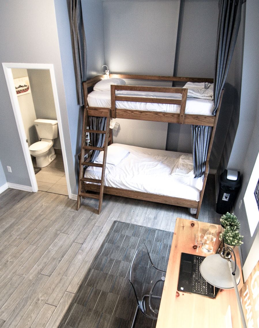 A bunk bed with a desk and chair, a small bathroom, and a trash bin.