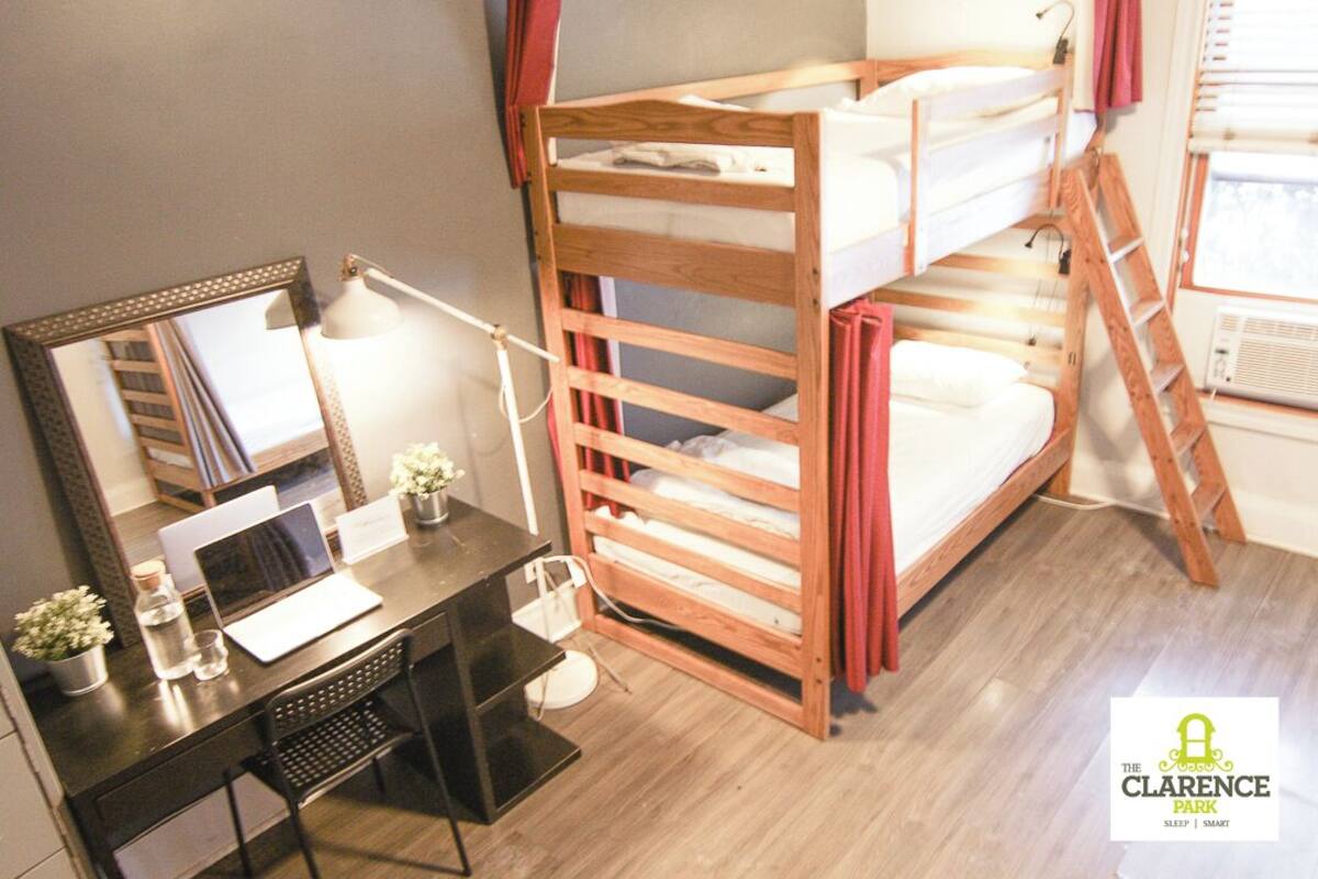 Een stapelbed met een ladder, een bureau met een laptop, een spiegel en een kleine plant.