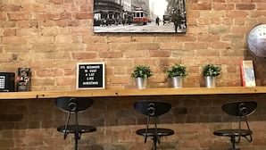 Un mur de briques sur lequel est apposée une plaque indiquant « Clarence Castle, Toronto, Canada », ainsi qu’une vieille photo des rues de Toronto. En dessous, on trouve une étagère avec des plantes en pot et une affiche sur le thème de Noël.