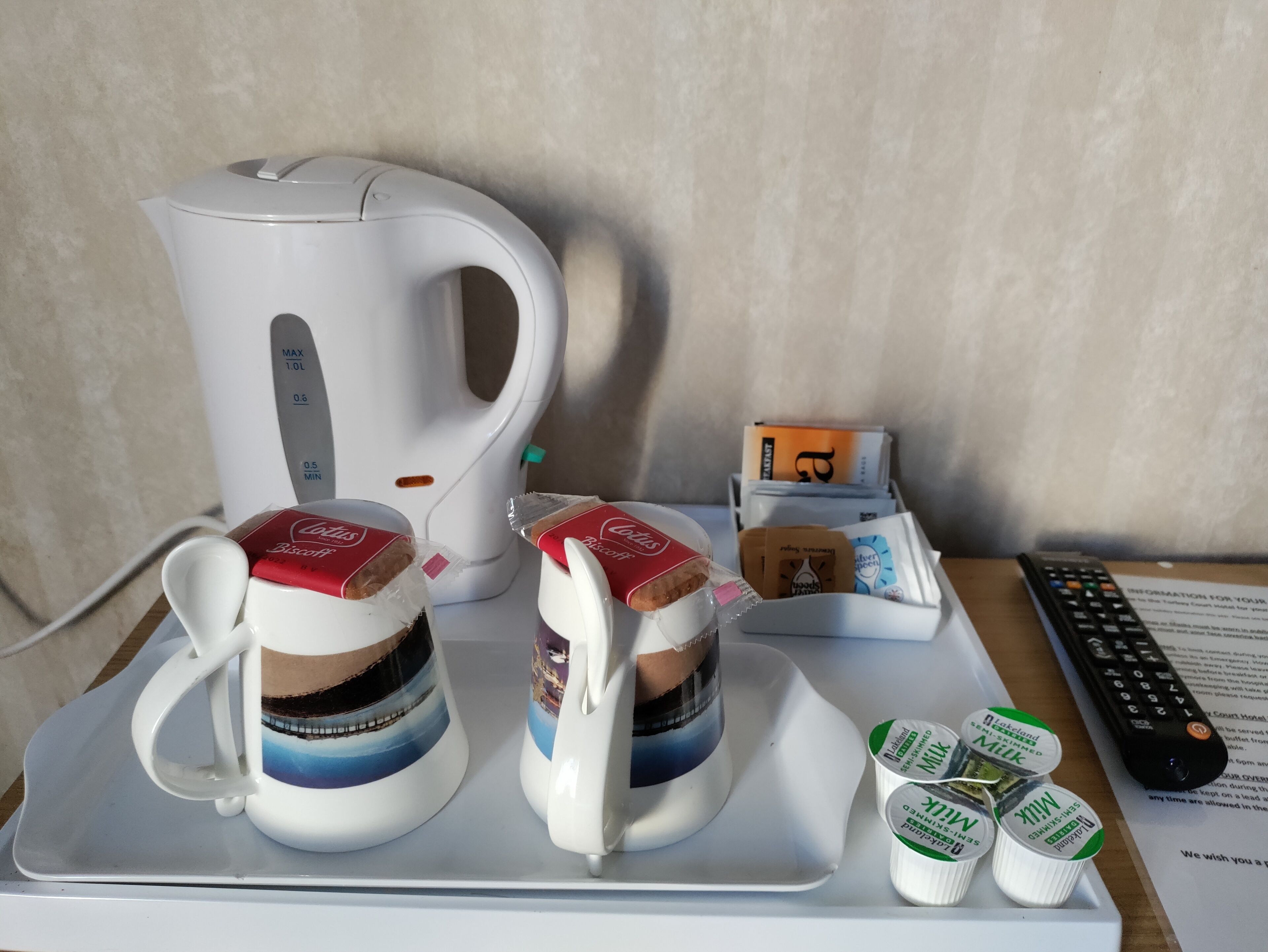 Une machine à café, deux tasses accompagnées de biscuits secs, une télécommande et des briques de lait, le tout sur un plateau.