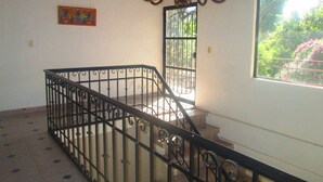 Una escalera con barandillas negras ornamentadas, un candelabro y una ventana con vistas a zonas verdes.