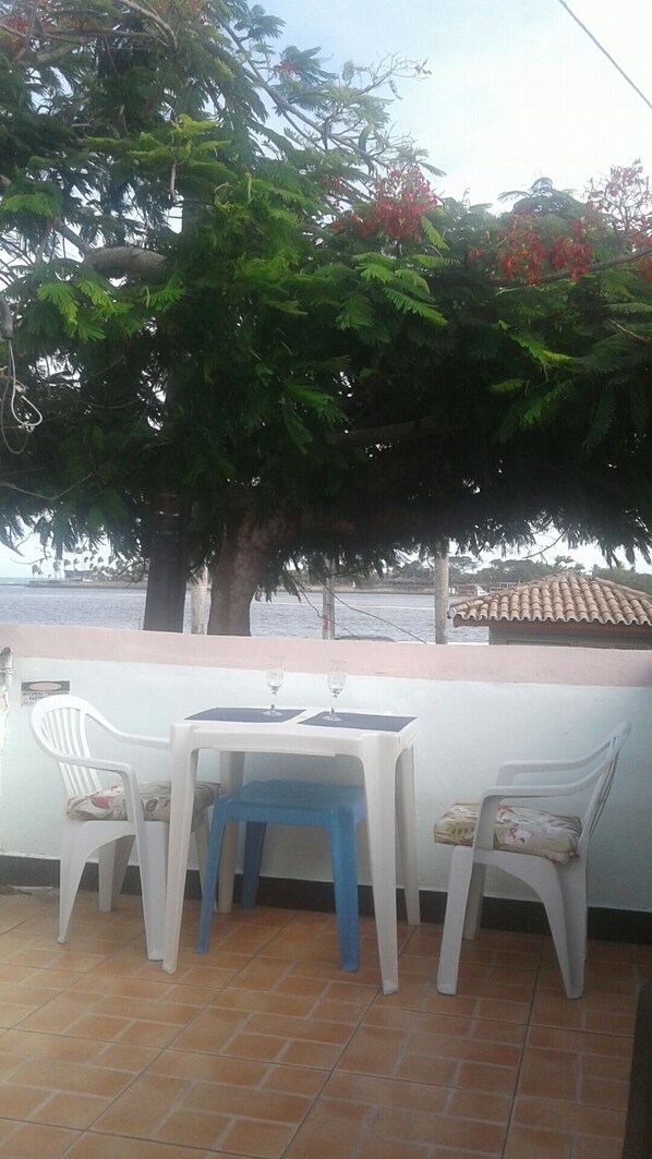 Une terrasse avec une table et des chaises, donnant sur une étendue d’eau et un bâtiment dont le toit est recouvert de tuiles.