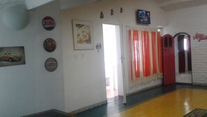 Un passadís amb una paret de maó blanc, una porta amb cortines vermelles, i un televisor muntat a la part superior.
