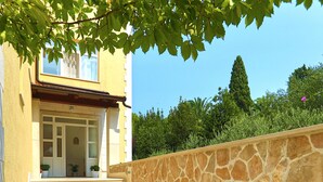 A staircase leading to a building entrance with a stone wall on one side and a tree providing shade. - Villa Malisko (Hvar)