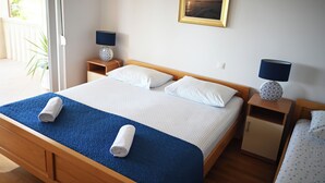 A neatly made bed with a blue blanket and two rolled towels, a wooden nightstand with a lamp, a small cabinet, and a framed picture on the wall. - Villa Malisko (Hvar)