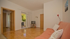 A living room with a wooden floor, a red sofa, a television, and a door leading to a balcony. - Villa Malisko (Hvar)