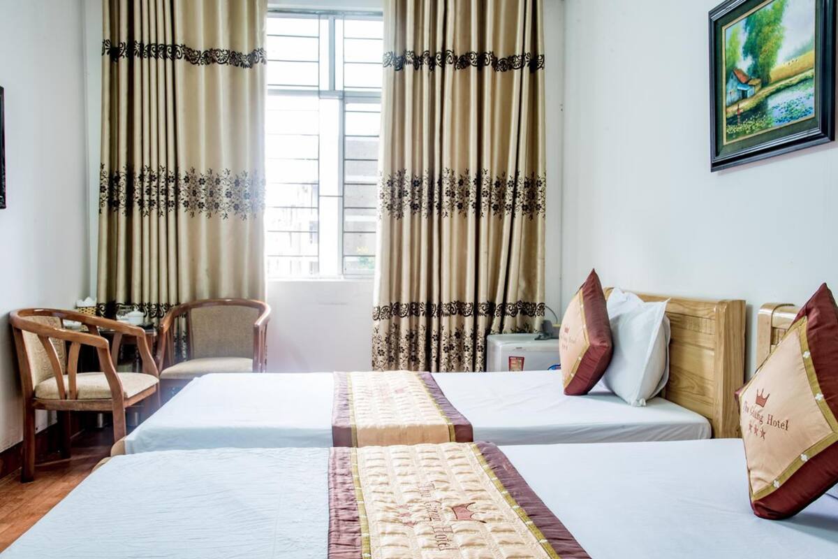 A hotel room with two beds, a chair, a nightstand, and curtains.