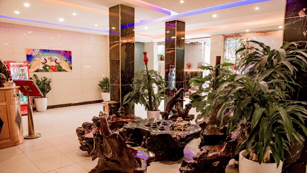 A lobby with a central wooden coffee table surrounded by potted plants, a Coca-Cola vending machine, and a large painting on the wall. - OYO 1143 Thu Giang Hotel (Hanoi)
