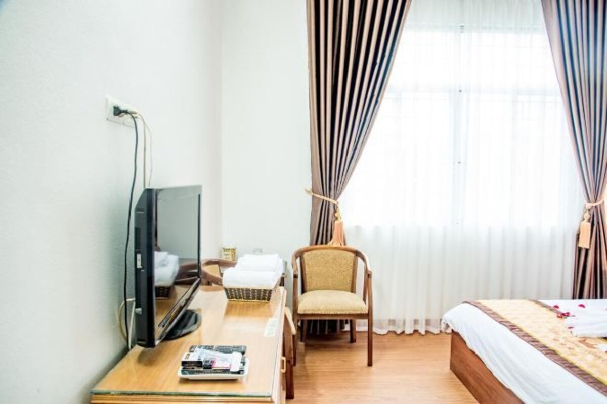 A hotel room with a bed, a desk with a television, a chair, and curtains.