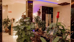 A lobby with a modern design, featuring a central wooden structure surrounded by large potted plants. - OYO 1143 Thu Giang Hotel (Hanoi)