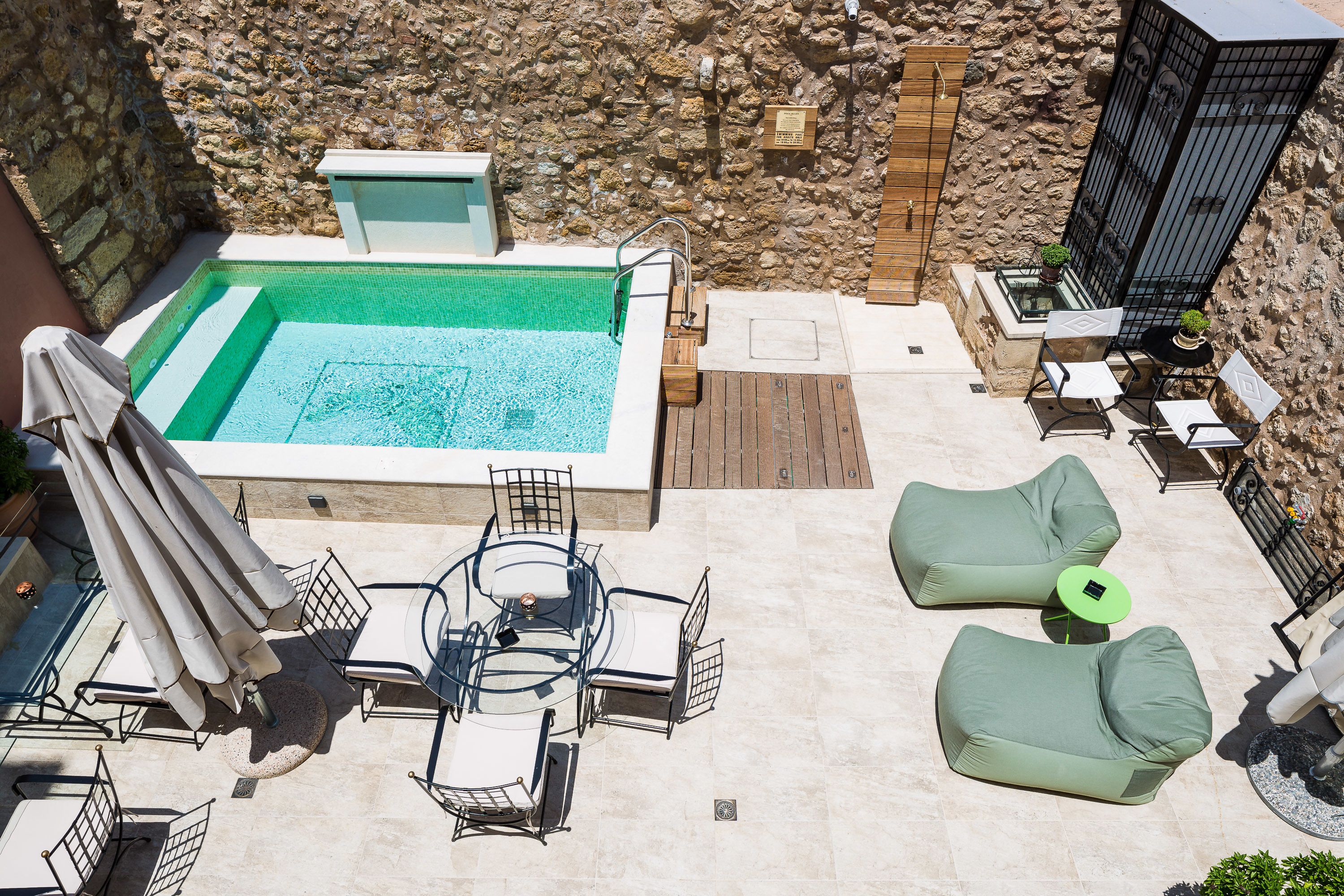 A rooftop pool area with a hot tub, lounge chairs, and a table with umbrellas.