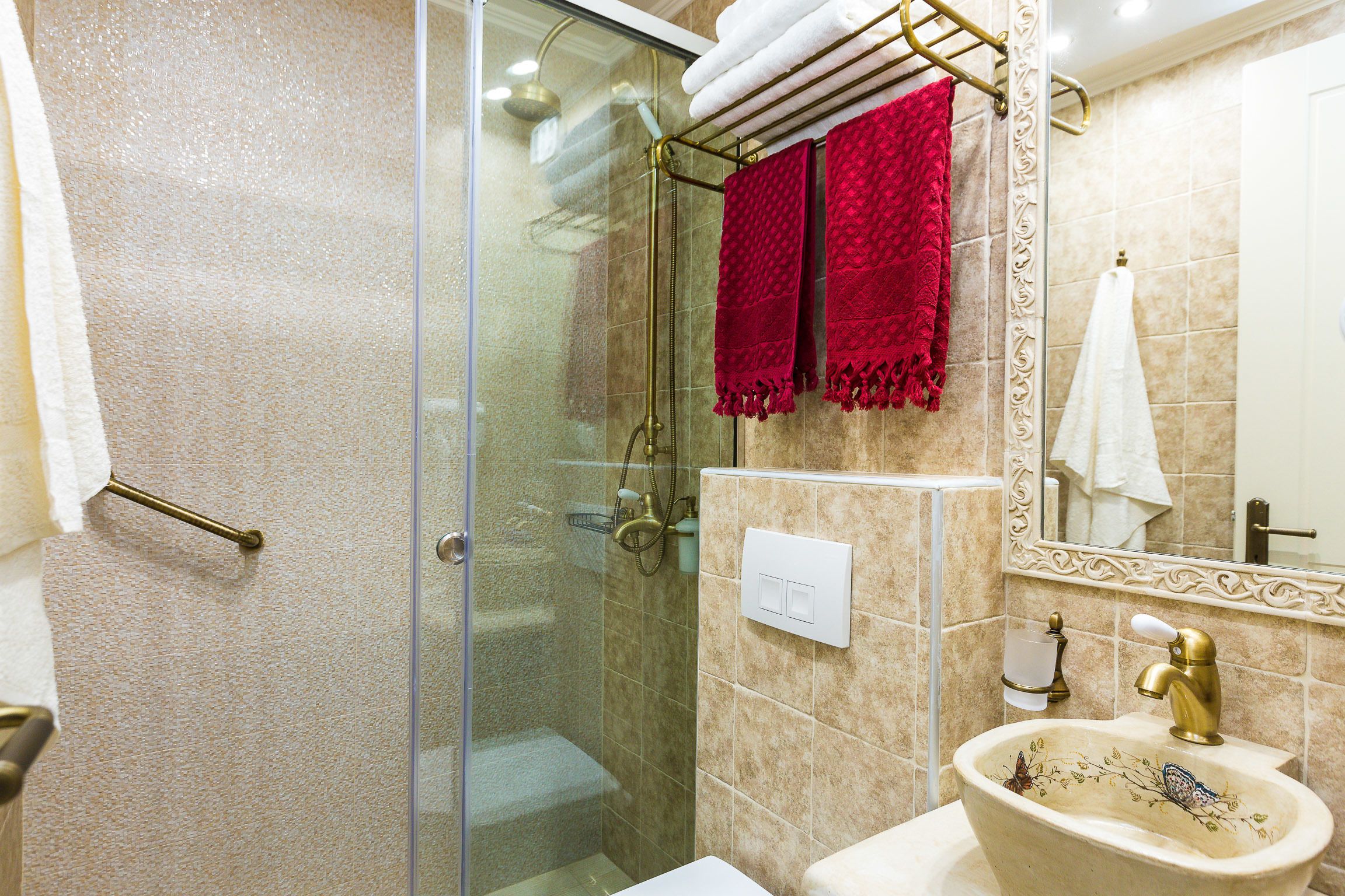 A bathroom with a glass-enclosed shower, a sink with a decorative basin, and two towels hanging on a rack.